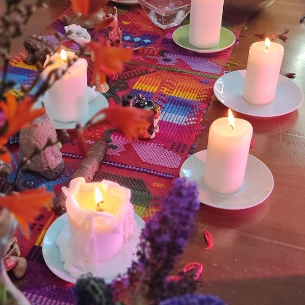 A close-up of a shamanic healing altar, featuring lit candles, vibrant flowers, and sacred objects on a colorful woven cloth.