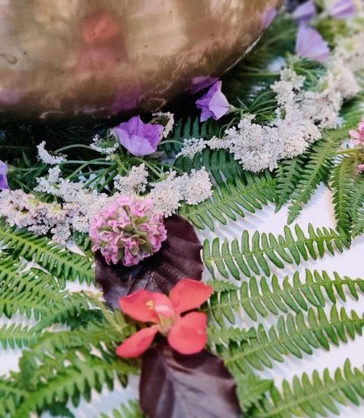 A sacred golden bowl holding pink petals, nestled among green ferns and delicate flowers, forming a spiritual altar.