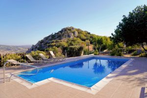 Outdoor pool with lounge chairs, surrounded by greenery and set against a scenic rocky hill under a clear blue sky.