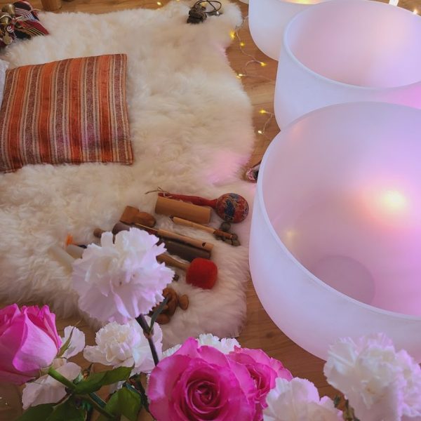 A cozy spiritual space with crystal singing bowls, a soft sheepskin rug, flowers, and ritual items arranged for a healing ceremony.