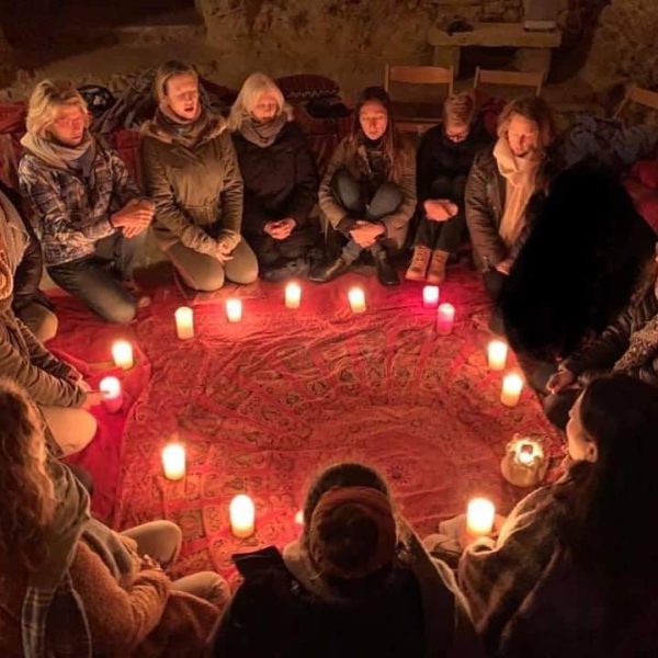 A group of women sitting in a circle, meditating around a ring of candles during a Full Moon & shamanic ceremony.