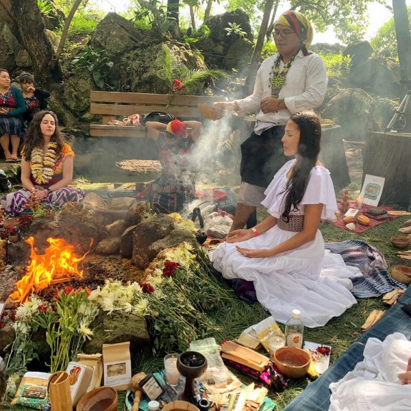 Carolina of Luminous Five participates in a sacred cacao initiation ceremony in a forest setting, surrounded by her maestro and spiritual guide, ceremonial fire, and sacred offerings.