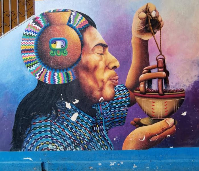 A vibrant mural in Guatemala, depicting an indigenous person wearing traditional clothing and holding a ceremonial incense burner, expressing cultural pride and spiritual connection.