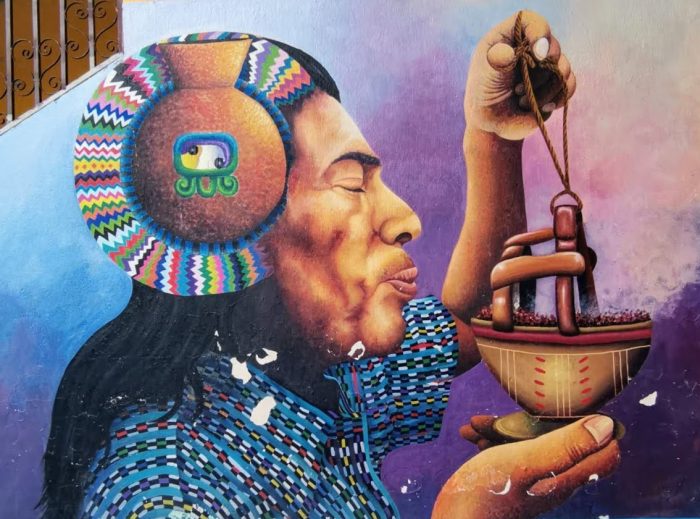 A vibrant mural in Guatemala, depicting an indigenous person wearing traditional clothing and holding a ceremonial incense burner, expressing cultural pride and spiritual connection.